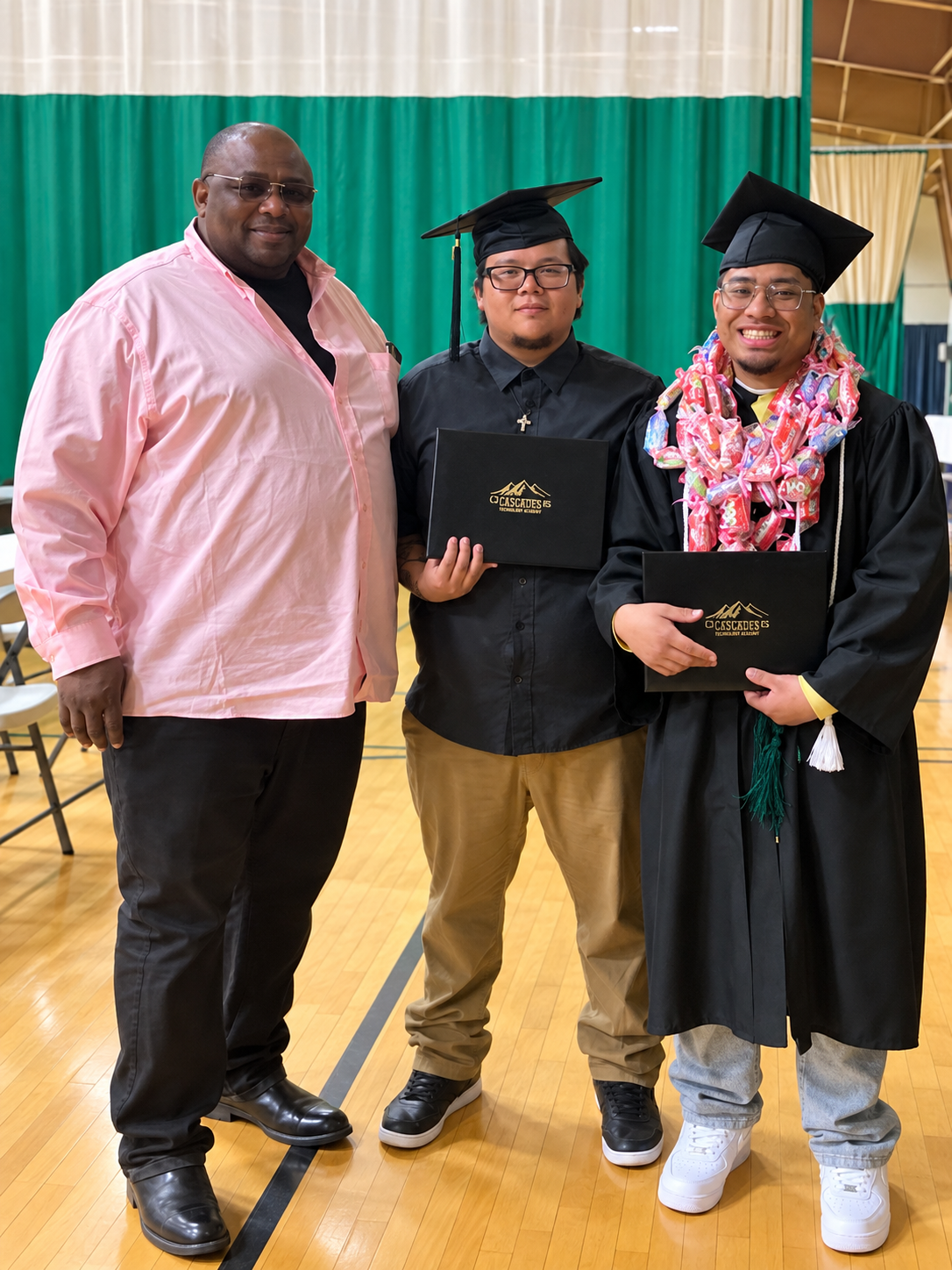 Lamont Hampton standing with two graduates at a graduation ceremony