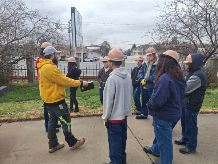 Hampton addressing a group of young people wearing hard hats outdoors
